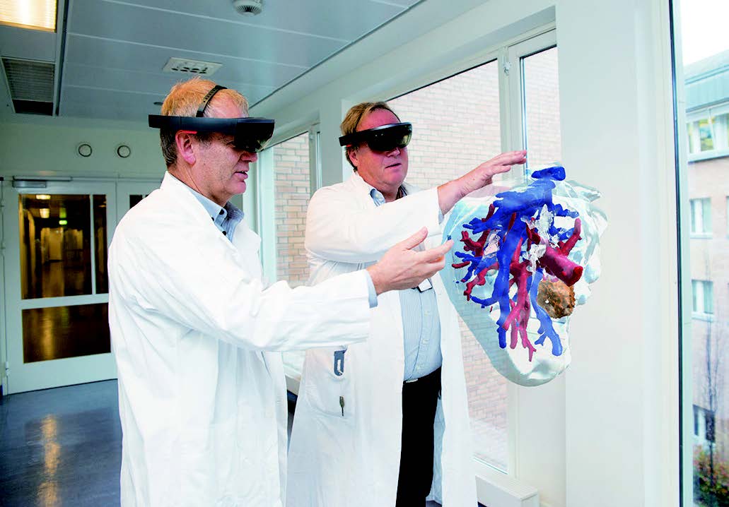 图 4：  脏模型的图片以及通过微软 HoloLens 查看时的显示方式。医学控制论和图像处理负责人 Ole Jakob Elle（左）和奥斯陆大学医院干预中心的外科医生 Bjørn Edwin（右）展示了正在研究协同操作规划的增强现实技术。图片由 Hanne Kristine Fjellheim / Sopra Steria 提供。