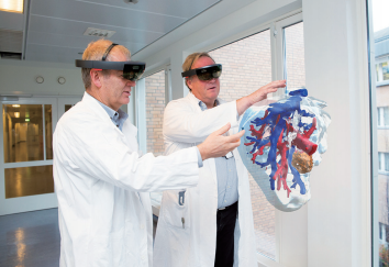 图 4：肝脏模型的图片以及通过 Microsoft HoloLens 查看时的显示方式。医学控制论和图像处理负责人 Ole Jakob Elle（左）和奥斯陆大学医院干预中心的外科医生 BjørnEdwin（右）展示了正在研究协同操作规划的增强现实技术。（图片由 Hanne Kristine Fjellheim / Sopra Steria 提供。）